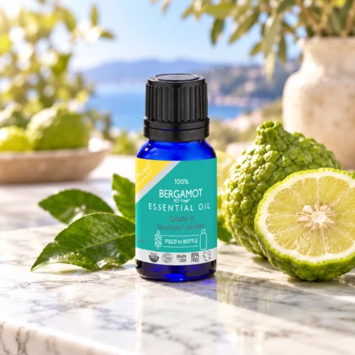 Chaé Bergamot Essential Oil on a white marble counter beside fresh green bergamots