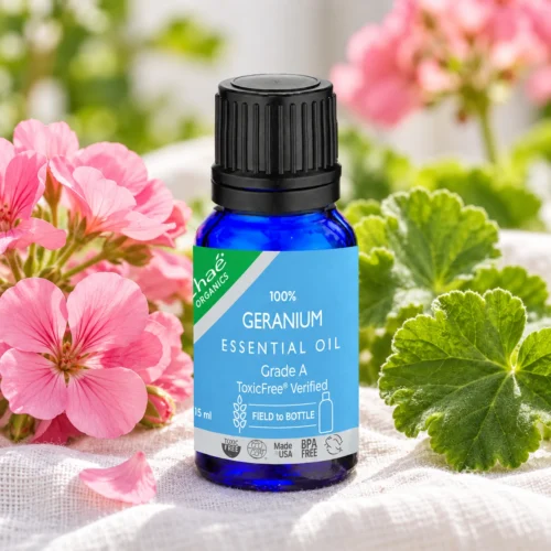 Chaé Geranium Rose Essential Oil on white linen with pink geranium flowers