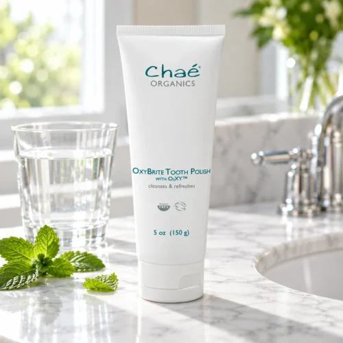 Chaé OxyBrite Tooth Polish on a marble bathroom counter with a glass of water and fresh mint