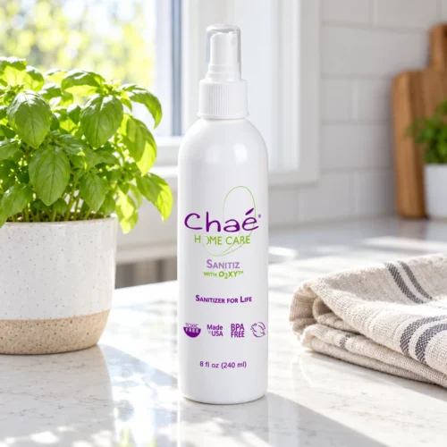 Chaé Sanitiz sanitizer spray on a kitchen counter with a basil plant and a tea towel