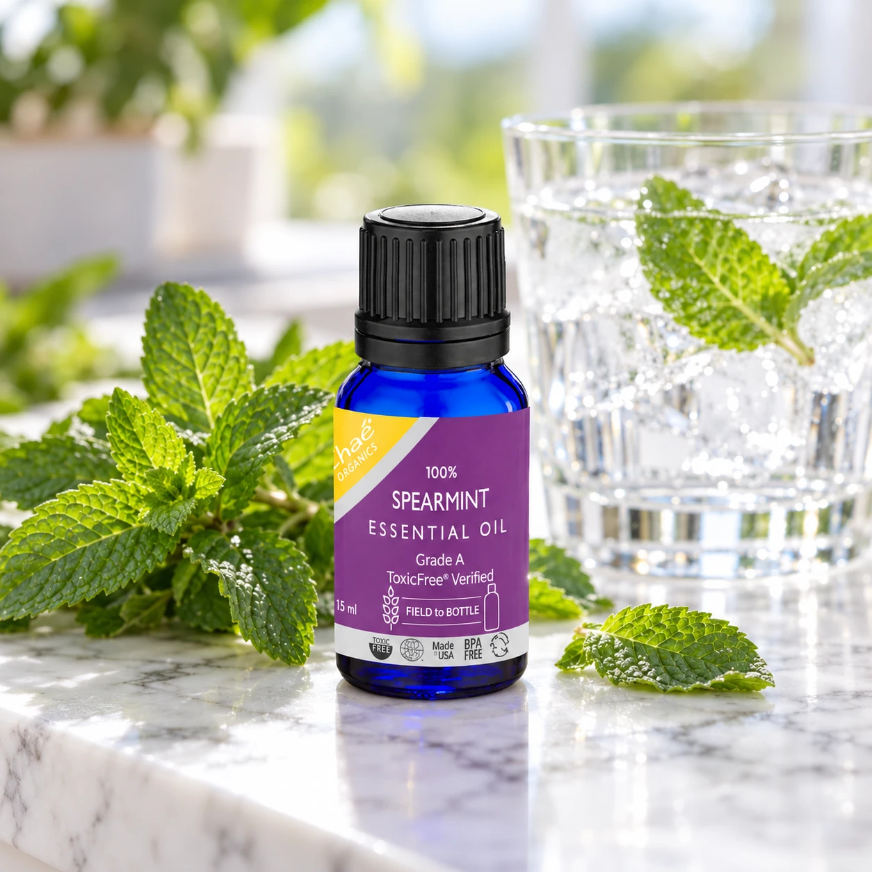 Chaé Spearmint Essential Oil in a blue 15 ml bottle on a marble counter beside fresh mint leaves