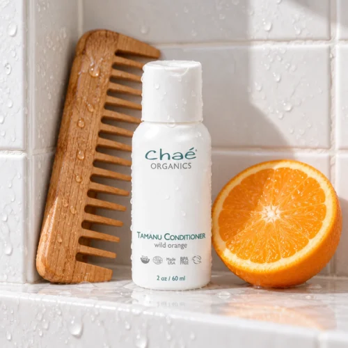 Chaé Tamanu Conditioner (Wild Orange) in a shower niche with a wooden comb and a fresh orange