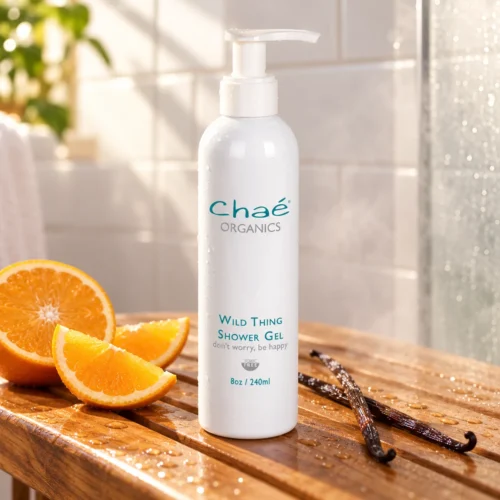 Chaé Wild Thing Shower Gel (Citrus & Vanilla) on a wooden shower bench with orange slices and vanilla pods