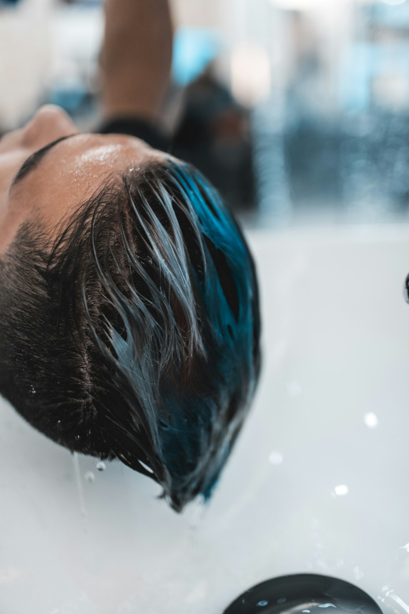 Freshly colored hair being rinsed at a salon sink, blue dye still visible in the wet strands